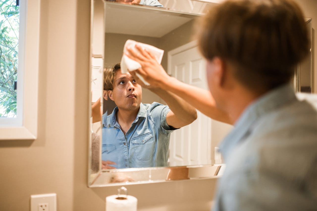 services-03 A man wiping a bathroom mirror, focusing on cleanliness and hygiene in a domestic setting.