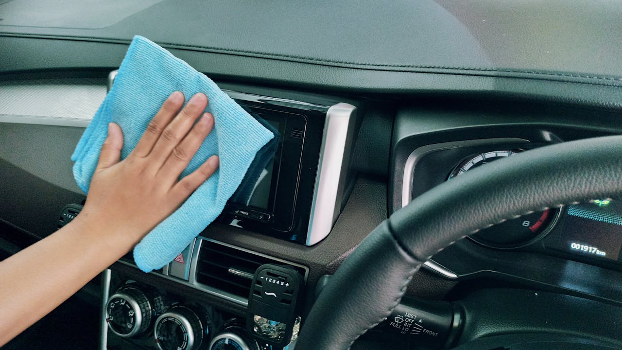 about-01 Close-up of a hand cleaning a car dashboard with a blue microfiber cloth.
