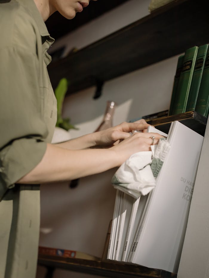 why-choose-us-03 Close-up of a person cleaning a bookshelf with a cloth in a home setting.